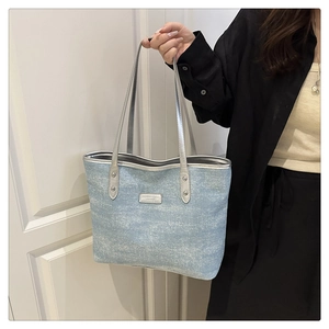 Detail of light blue glitter tote bag with silver handles and metal fashion logo plate