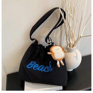 Detail of black nylon tote with BEACH print and cute plush bread charm on the strap