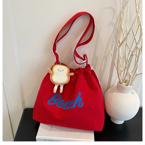 Detail of red drawstring canvas tote with blue Beach print and bread plush charm