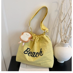 Detail of yellow nylon drawstring tote bag with Beach print and cute toast plush charm