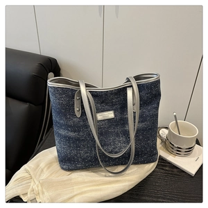 Detailed close-up of a blue denim tote bag with silver leather trim and metal logo plate