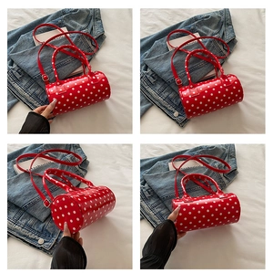 Detailed close-up of red and white polka dot cylindrical handbag showing shiny texture