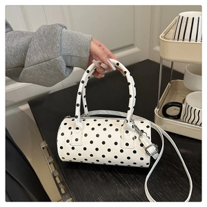 Close-up of white leather barrel bag featuring black polka dots and dual top handles