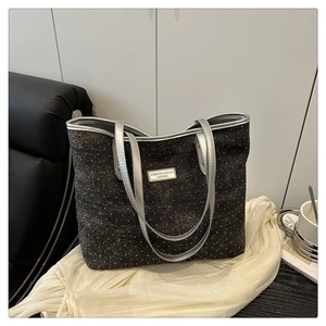 Detail of silver brand plate on dark grey polka dot tote bag with leather piping