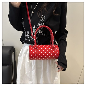 Close-up of a red polka dot barrel bag in glossy patent leather with top handles