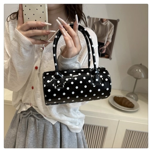 Close-up of a glossy black and white polka dot cylinder handbag held by a model