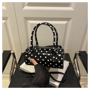 Detailed view of polka dot cylindrical handbag in glossy patent leather on a white book