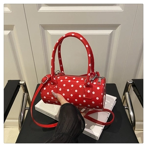 Detailed view of red polka dot cylinder handbag with glossy finish on prop book