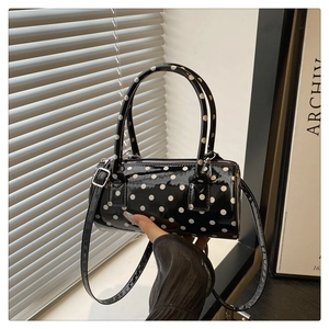 Close-up of a glossy polka dot cylinder bag with dual handles and silver hardware detail