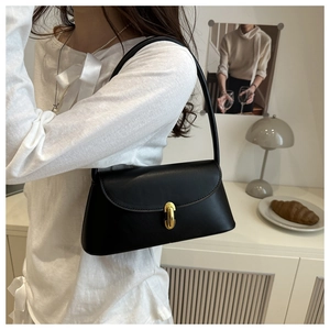 Detail of black vintage shoulder bag with golden oval clasp worn by a model in lifestyle setting