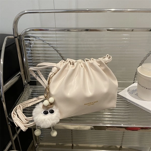 Creamy white drawstring bucket bag with plush charm on modern decorative glass shelf