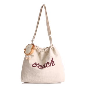 Cream canvas drawstring tote bag with red Beach lettering and cute toast plush charm