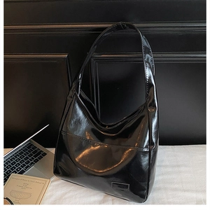 Detail of black glossy tote bag featuring a front pocket, shown with a laptop in a workspace
