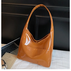 Detail view of glossy brown leather shoulder bag with decorative front pocket on white desk