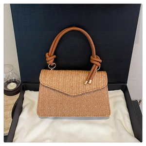 Détail du tissage et du rabat en V d'un sac bandoulière marron dans une boîte cadeau