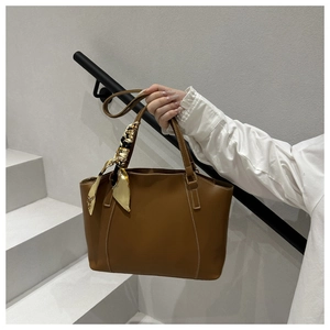 Brown leather tote bag with a yellow patterned scarf tied on the handle at a staircase