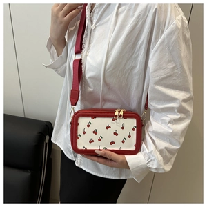 Detail showing white crossbody bag with red cherry patterns and gold zipper on a model