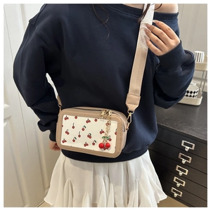 Detail of white canvas crossbody bag with red cherry prints and wide fabric strap