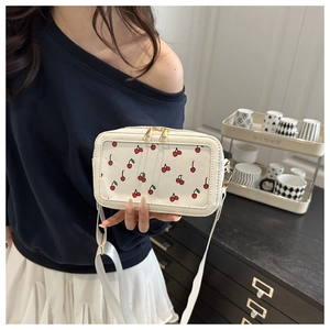 Close-up of white crossbody bag featuring red cherry patterns and transparent window
