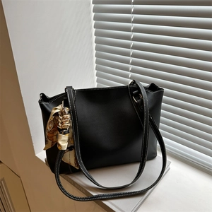 Minimalist black leather tote bag with white contrast stitching and a patterned silk scarf