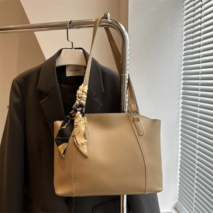 Minimalist beige leather tote bag with printed silk scarf on a metal hanger