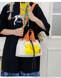 Detail of color-block nylon crossbody bag with orange handles and drawstring closure