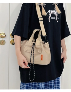 Detail of beige nylon crossbody bag with drawstring closure and orange woven brand tag