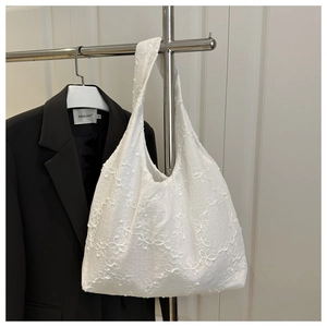 Détail du sac cabas blanc présentant une broderie florale délicate et un tissu texturé