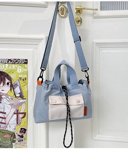 Detailed view of blue nylon crossbody bag with beige pocket hanging on a door handle