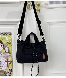 Detail of black nylon tote bag with orange label and drawstring closure on door handle