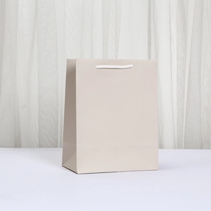 Detailed view of beige paper gift bag with white rope handles and minimalist design