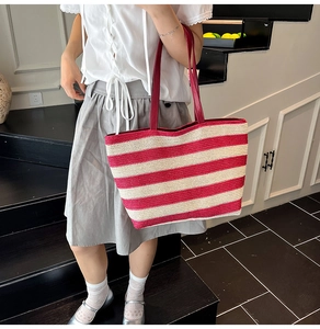Détail du grand sac cabas en paille à rayures rouges et blanches porté par un mannequin