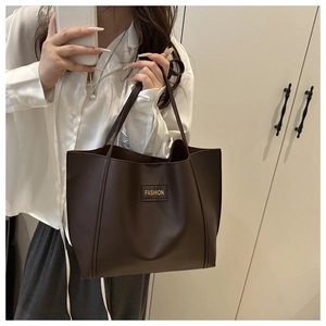 Detail of deep brown faux leather tote bag with gold fashion label held by a model