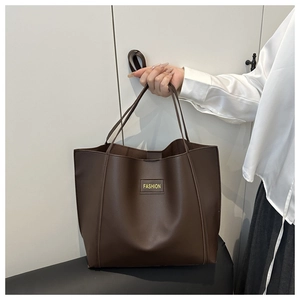 Close-up of a dark brown tote bag with a fashion label held by a model in a studio