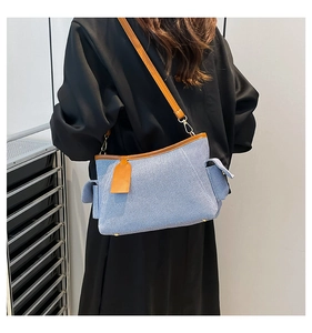 Close-up of a blue denim shoulder bag with brown leather trim and side pocket detail