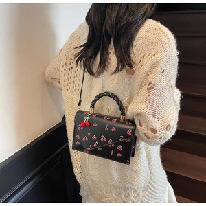 Mannequin portant un sac bandoulière noir brodé cerise avec poignée torsadée sur pull blanc