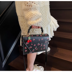 Detail of black crossbody bag with red cherry prints and woven handle on stairs