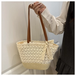 Detail of a cream lace tote bag with brown leather straps and a decorative side bow