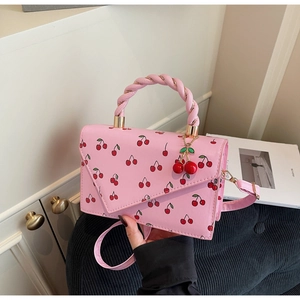 Detailed close-up of pink cherry print handbag with twisted handle and cherry pendant