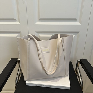 Large beige leather tote bag with FASHION patch on a metal chair in a stylish room