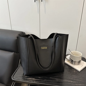 Large black leather tote bag with FASHION label on minimalist dark wooden table