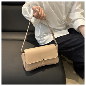 Detail of a beige leather shoulder bag with a gold U-shaped clasp held by a model