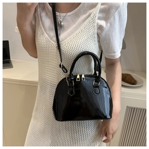 Glossy black patent leather shell bag shown with adjustable strap in lifestyle setting