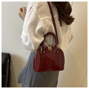 Model showing a burgundy patent leather shell bag with gold hardware and shoulder strap