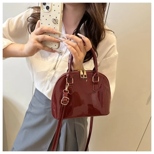 Close-up of a burgundy patent leather shell bag with gold hardware and top handle