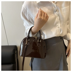 Detail of dark brown glossy shell bag with gold hardware on a model's shoulder