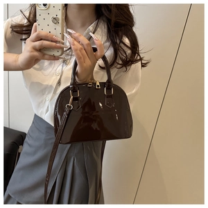 Detail of the glossy dark brown shell bag with a zipper and golden metal hardware