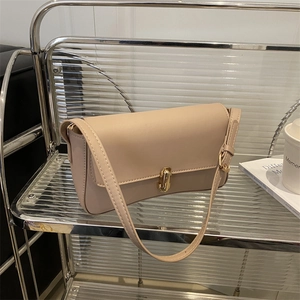 Minimalist beige baguette shoulder bag with elegant gold metal clasp on a modern shelf