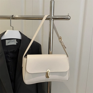 Minimalist beige leather shoulder bag with a gold metal clasp shown on a display stand