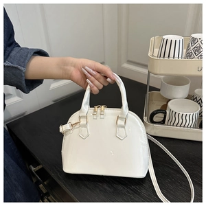 White patent leather shell bag with gold hardware held by hand in a modern interior